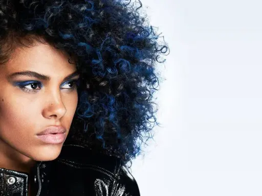 Mujer con cabello rizado negro azulado y maquillaje vibrante, luciendo una chaqueta brillante.