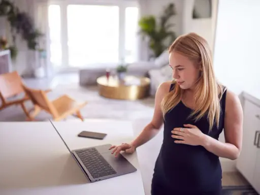 Ciężarna kobieta sprawdza na laptopie, czy skurcze co 20 minut oznaczają poród.