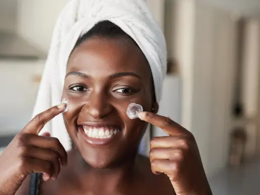 Sourire radieux, une femme applique une crème sur ses joues. Un avant-après prometteur pour une peau éclatante grâce au rétinol.