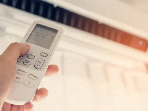 Mano ajustando el control remoto del aire acondicionado a 22 grados. ¿Cuántas frigorías por metro cuadrado necesita tu hogar para estar fresco?