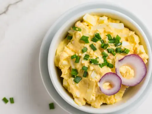 Pyszna pasta jajeczna z serem, posypana szczypiorkiem i ozdobiona krążkami czerwonej cebuli. Idealna na kanapki.