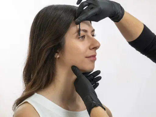 Une esthéticienne ajuste les sourcils d'une femme avec une brosse, préparant un browlift pour un regard sublimé.