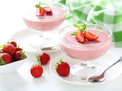 Deliziosa mousse di fragole in coppette di vetro, guarnita con fragole fresche e menta. Accanto, fragole in una ciotola bianca.