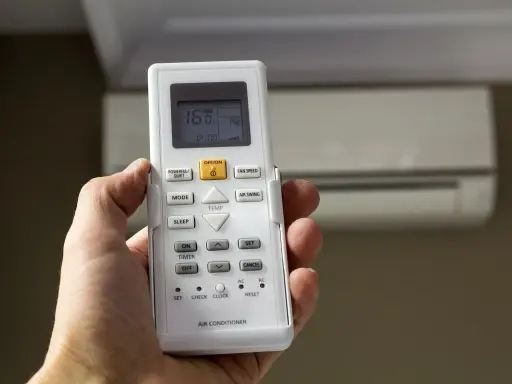Mano sujetando mando para configurar mando universal aire acondicionado sin código. Aire acondicionado al fondo.