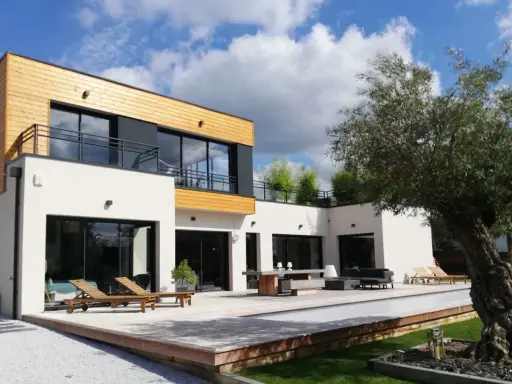 Maison moderne avec un style architectural audacieux, mêlant bois et blanc. Terrasse spacieuse avec mobilier extérieur et piscine.
