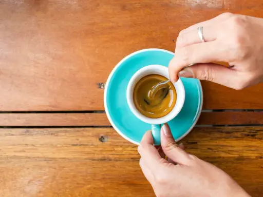 Mani che mescolano un caffè, nonostante si dica che il caffè è cancerogeno, il suo aroma attira.