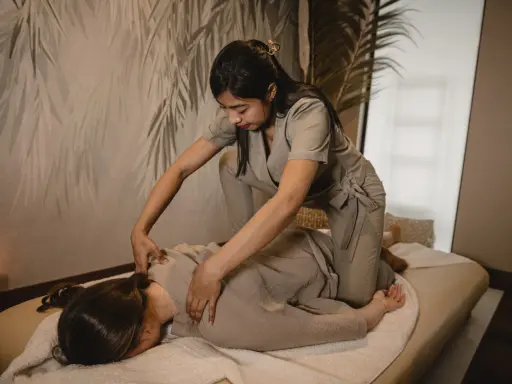 Relaksacyjny shiatsu masaż pleców. Terapeuta klęczy obok klienta leżącego na macie, wykonując delikatne naciski.