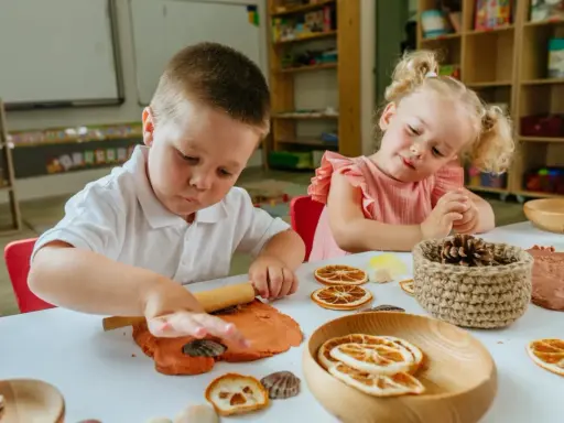 Niños de 3 a 4 años disfrutan de actividades creativas en casa, moldeando arcilla y decorando con elementos naturales.