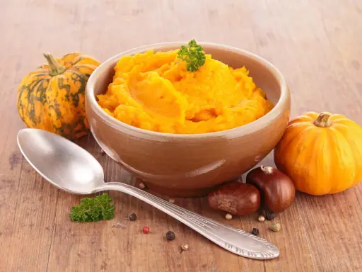 Miseczka z puree z dyni, obok dynie i łyżka. Idealne na jesienne dania, co zrobić z puree z dyni?