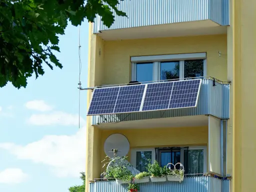 Två solceller monterade på en balkong på ett gult flerfamiljshus. Gröna växter i krukor på den nedre balkongen.