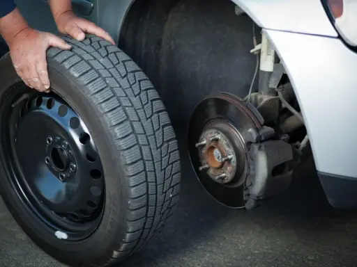 Mani che cambiano una gomma invernale, rispettando l'obbligo cambio gomme per la sicurezza stradale.
