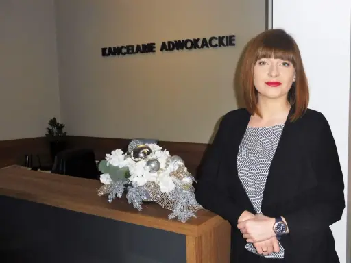 Kobieta w czarnym żakiecie przy recepcji z dekoracją kwiatową. Napis "KANCELARIE ADWOKACKIE".