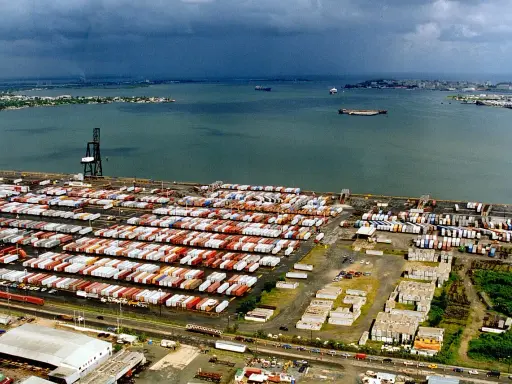 Vasto deposito di container nel porto di San Juan, Porto Rico, con navi in lontananza sotto un cielo nuvoloso.