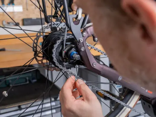 Hand löst Kette, um Nabenschaltung Hinterrad auszubauen. Werkzeug liegt bereit.