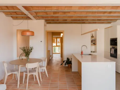 Comedor y cocina luminosos en una casa vieja decorada con poco dinero. Techos de vigas de madera y baldosas de terracota.