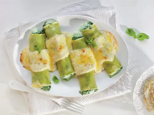 Pyszne cannelloni ze szpinakiem, zapieczone pod kremowym sosem serowym, ozdobione listkami bazylii.