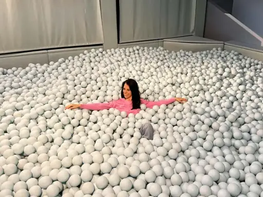 Mujer sonriente se sumerge en una piscina de bolas blancas, un divertido ikono madrid.