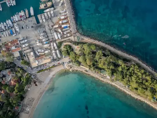 Widok z lotu ptaka na port i plażę w Kemerze. Widać liczne jachty i łodzie, a także zielony teren z drzewami. To idealne miejsce na odkrywanie atrakcji Kemer Turcja.