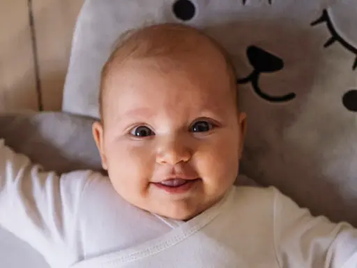 Uśmiechnięte niemowlę w białym body leży na miękkiej poduszce w kształcie misia. To mądre imię dla chłopca, które przyniesie mu szczęście.