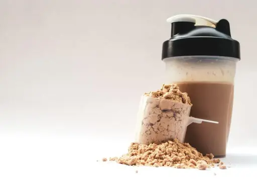Ein Löffel Proteinpulver neben einem fertigen Proteinshake im Shaker. Perfekt für den proteinreichen Start in den Morgen.