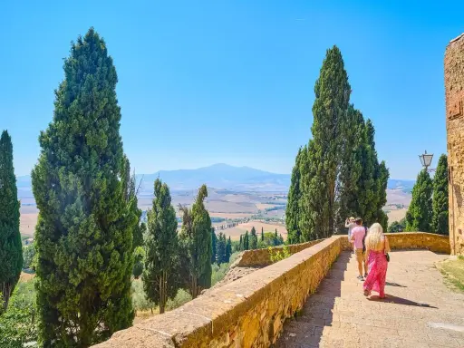 Coppia in cammino durante un tour Toscana 5 giorni, tra cipressi e colline ondulate sotto un cielo azzurro.