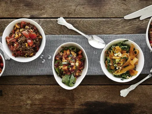 Verschiedene Salate als Beilagen für ein Fondue: Linsensalat, Gemüsesalat mit Karotten und Grünkohl, sowie ein weiterer bunter Salat.