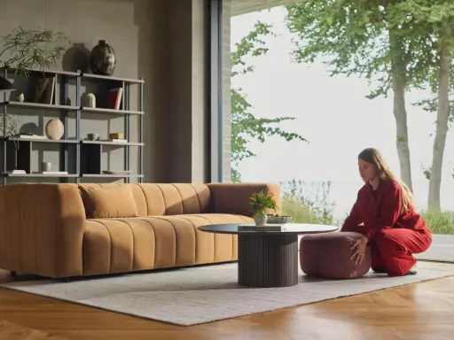 En kvinna i rött sitter på en pall bredvid en orange soffa. En dansk designer kan ha skapat detta stilrena vardagsrum.