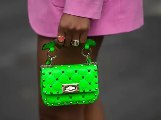 Borsa verde neon, colore complementare del fucsia, con borchie dorate e catena. Indossata da una mano con anelli.