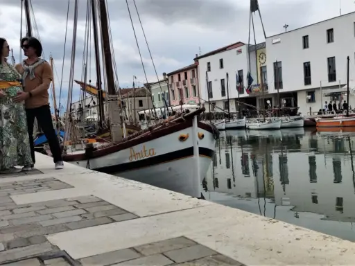 Coppia in attesa a Cesenatico, con barche d'epoca ormeggiate e il Municipio sullo sfondo. Un ricordo speciale prima di San Marino.