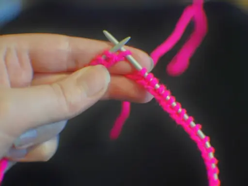 En hand håller stickor och ljusrosa garn, redo att starta stickning.