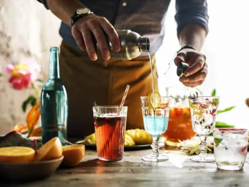 Barman przelewa płyn z shakera do drinka, tworząc kolorowe koktajle. Mieszanie alkoholi to sztuka.
