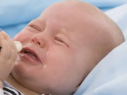 Ein weinendes Baby mit geschlossenen Augen, dem eine Flasche angeboten wird. Das Baby will nicht trinken.