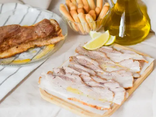 Chicharrón de Cádiz, lonchas de panceta crujiente, limones y palitos de pan, listos para disfrutar.