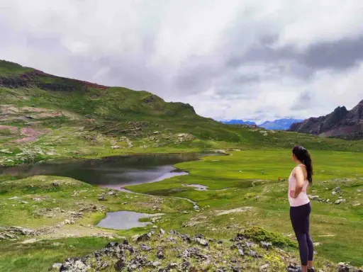 Mujer admira un lago y prados verdes en el Valle de Tena, ideal para rutas de senderismo.