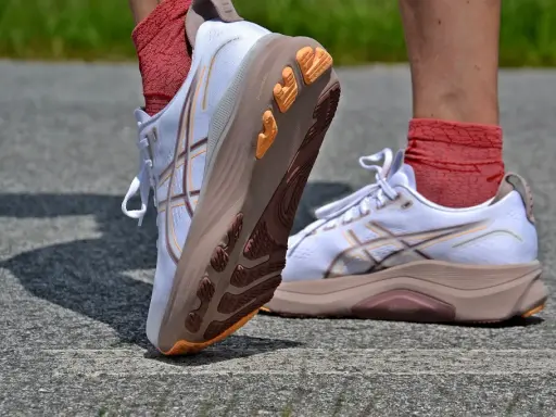 Białe buty do biegania z pomarańczowymi akcentami i charakterystycznym logo. To właśnie asics co to za firma, znana z innowacyjnych rozwiązań dla sportowców.