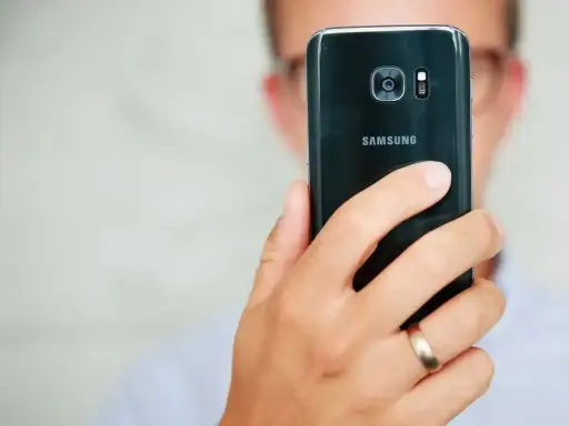 Osoba trzyma czarny telefon Samsung, pokazując tył z aparatem. Dowiedz się, jak poprawić jakość aparatu w telefonie Samsung, aby robić lepsze zdjęcia.