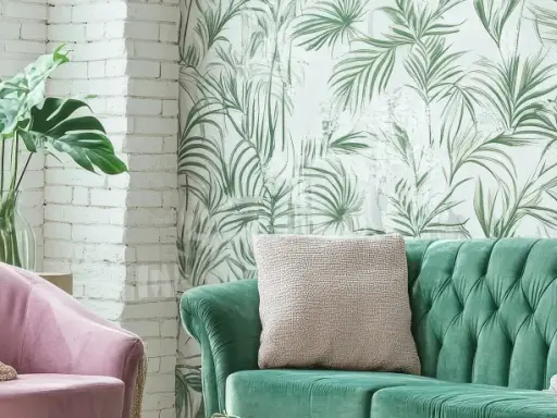 Ein grünes Samtsofa und ein rosafarbener Sessel mit einer Monstera-Pflanze. Die Wand hinter dem Sofa ist mit einer tropischen Tapete mit Palmenblättern dekoriert, eine tolle Idee, um zwei Tapeten zu kombinieren.