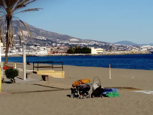 Sonniger fuengirola strand mit Palmen, Bergen und dem Meer im Hintergrund. Kinderwagen und Gepäck liegen am Sand.