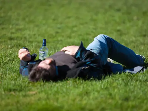 Mężczyzna leży na trawie obok butelki wódki. Czy padaczka alkoholowa jest śmiertelna? To pytanie budzi niepokój.