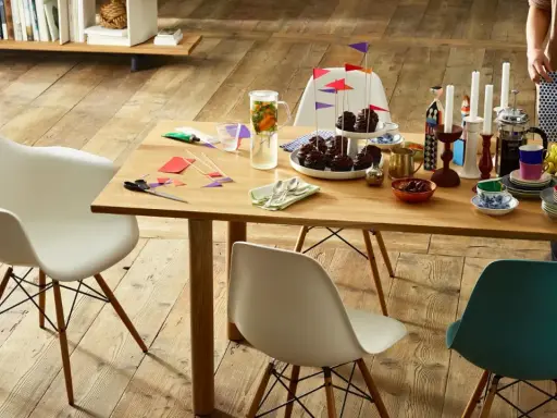 Tavolo in legno con sedie Eames House, cupcake, candele e fiori. Un'atmosfera accogliente per una festa.