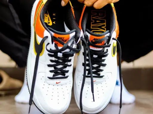 Białe buty Nike Air Force 1 z pomarańczowo-żółtymi akcentami. Sprawdź metkę i logo, by dowiedzieć się, jak sprawdzić czy buty są oryginalne.