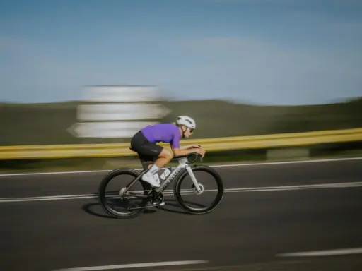 Kolarz w fioletowej koszulce pędzi na rowerze, osiągając prędkość 50 km/h.