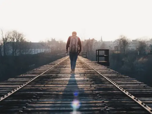 En person med ryggsäck går ensam på en gammal järnvägsbro i solnedgången, en bild som kan symbolisera ett bakslag vid utmattningssyndrom.