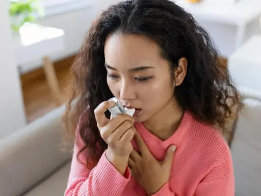 Junge Frau mit Asthma benutzt ihren Inhalator, der Cortison enthält, um ihre Atemwege zu öffnen.