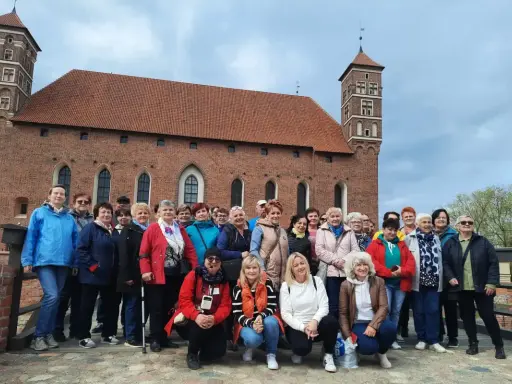 Grupa turystek pozuje na tle imponującego zamku biskupów warmińskich w Lidzbarku Warmińskim.