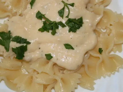 Makaron farfalle polany kremowym sosem serowym i posypany natką pietruszki.