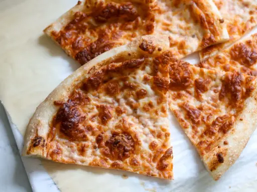 Tranches de pizza au fromage doré, préparées avec un levain rafraichi, sur du papier sulfurisé.