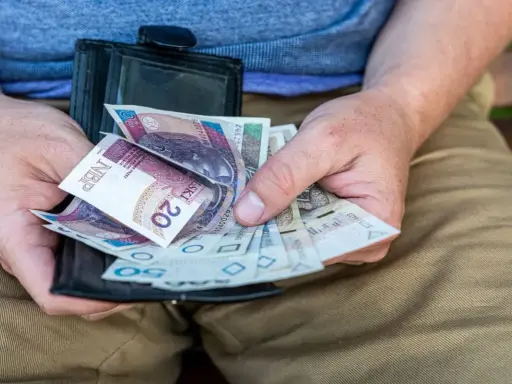 Ręce trzymają portfel z polskimi banknotami. Czy dodatek pielęgnacyjny jest opodatkowany? Pieniądze w portfelu mogą pomóc w odpowiedzi.