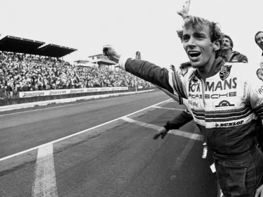 Jubelnder Stefan Bellof im Rennanzug mit "Le Mans" und "Porsche" Aufschrift, jubelnde Menge im Hintergrund.