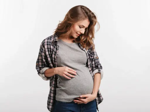 Kobieta w ciąży delikatnie dotyka brzucha. Częste oddawanie moczu w ciąży to normalny objaw.